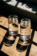 Two shot glasses with water labeled 'All people deserve love' and 'Enjoy the little things' on a wooden surface.