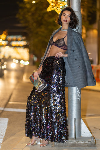 Woman in evening gown and coat standing on a street at night.