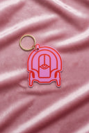 This image features a vibrant pink plastic keychain shaped like a carriage. The keychain has a gold-colored ring for attaching keys and a distinct, plush-like texture that enhances its visual appeal.
